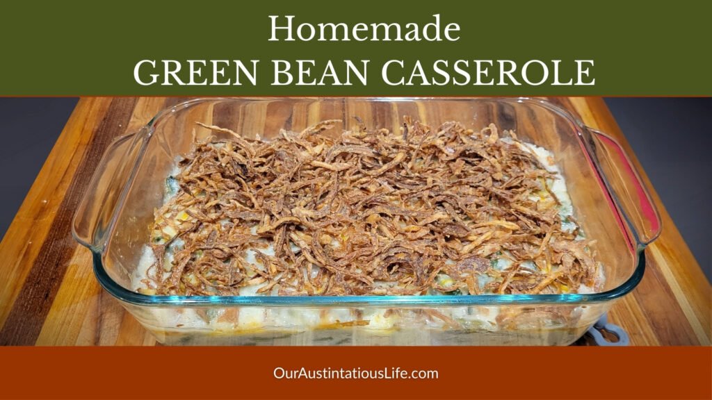 Homemade green bean casserole topped with crispy fried onions in a glass baking dish on a wooden cutting board.