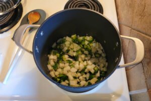 Chopped onions, jalapeños, and garlic cooking in a pot to start chicken pozole verde.