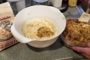 Cornbread stuffing being mixed into a bowl of masa for tamales.