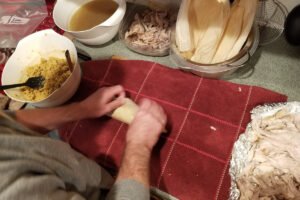 Hands folding a tamale before placing it into the steamer pot.