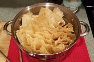 Cooked tamales standing upright in a metal colander after steaming.