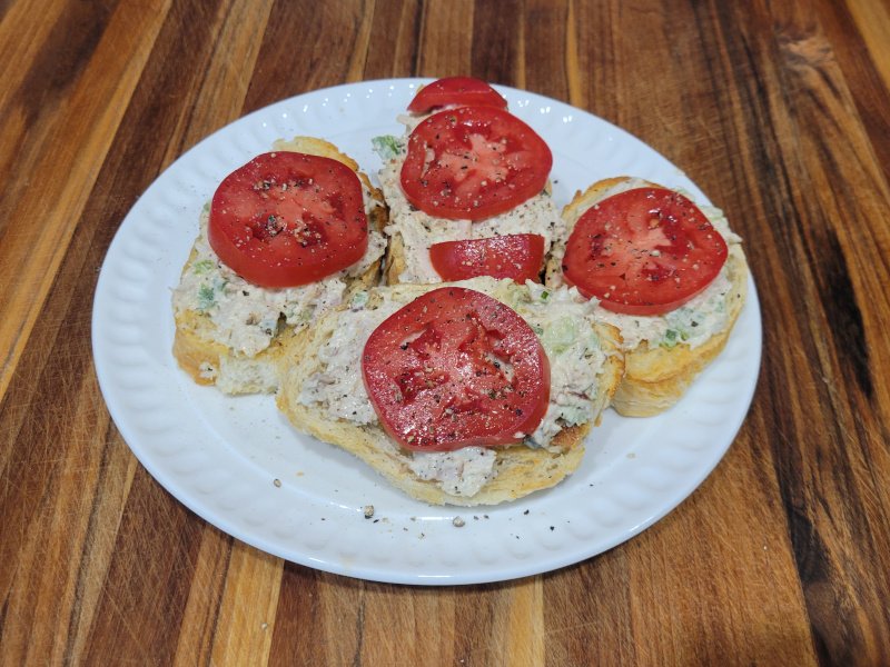 Turkey Salad Crostini with Tomato Turkey salad crostini on a white plate, topped with fresh tomato slices and cracked black pepper.
