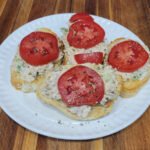 Turkey salad crostini on a white plate, topped with fresh tomato slices and cracked black pepper.