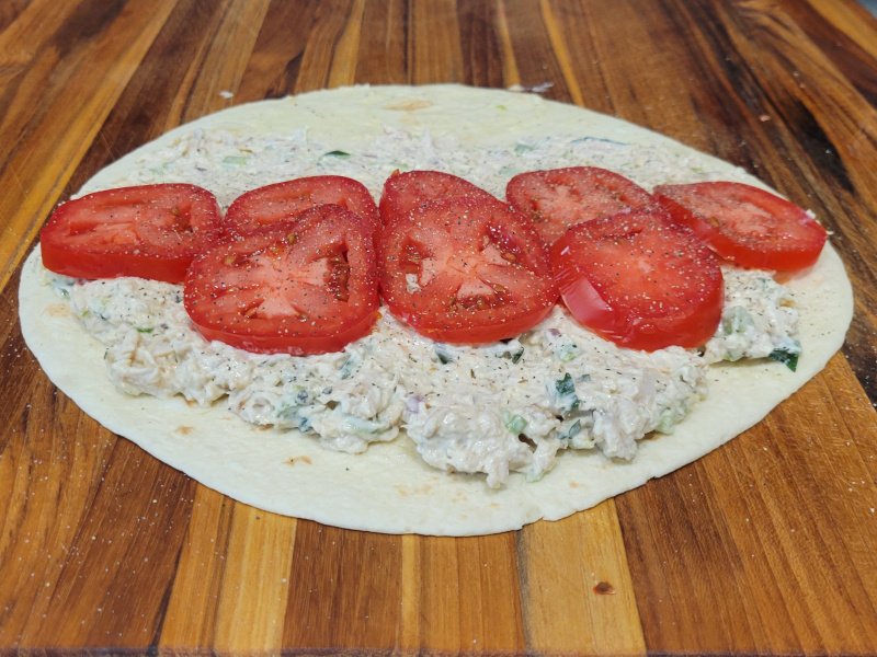 Turkey Salad Wrap – Step 2 Add Tomatoes Turkey salad on a tortilla topped with sliced tomatoes seasoned with black pepper.